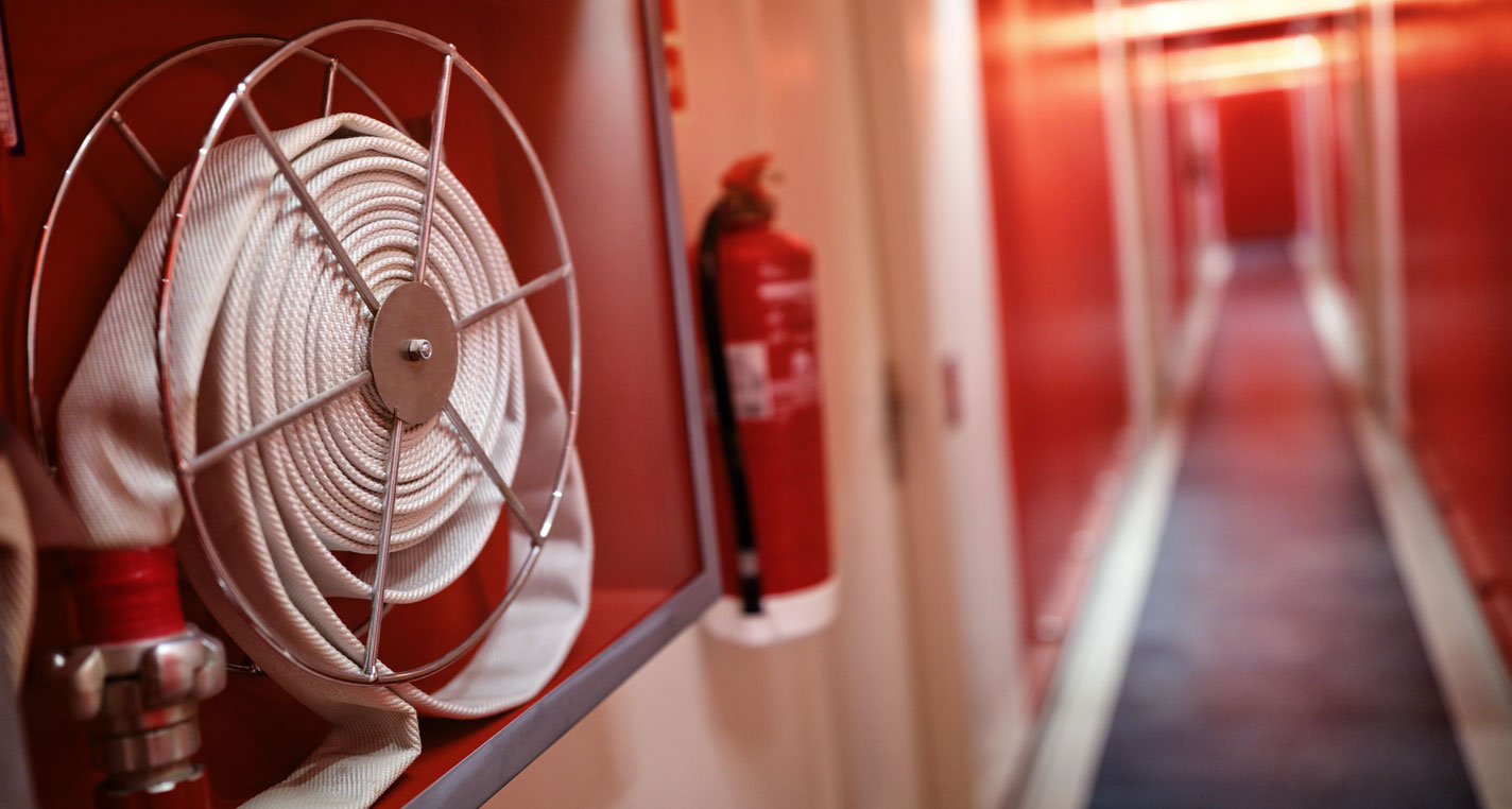 Mangueira e extintor de incêndio instalados em corredor de edificação